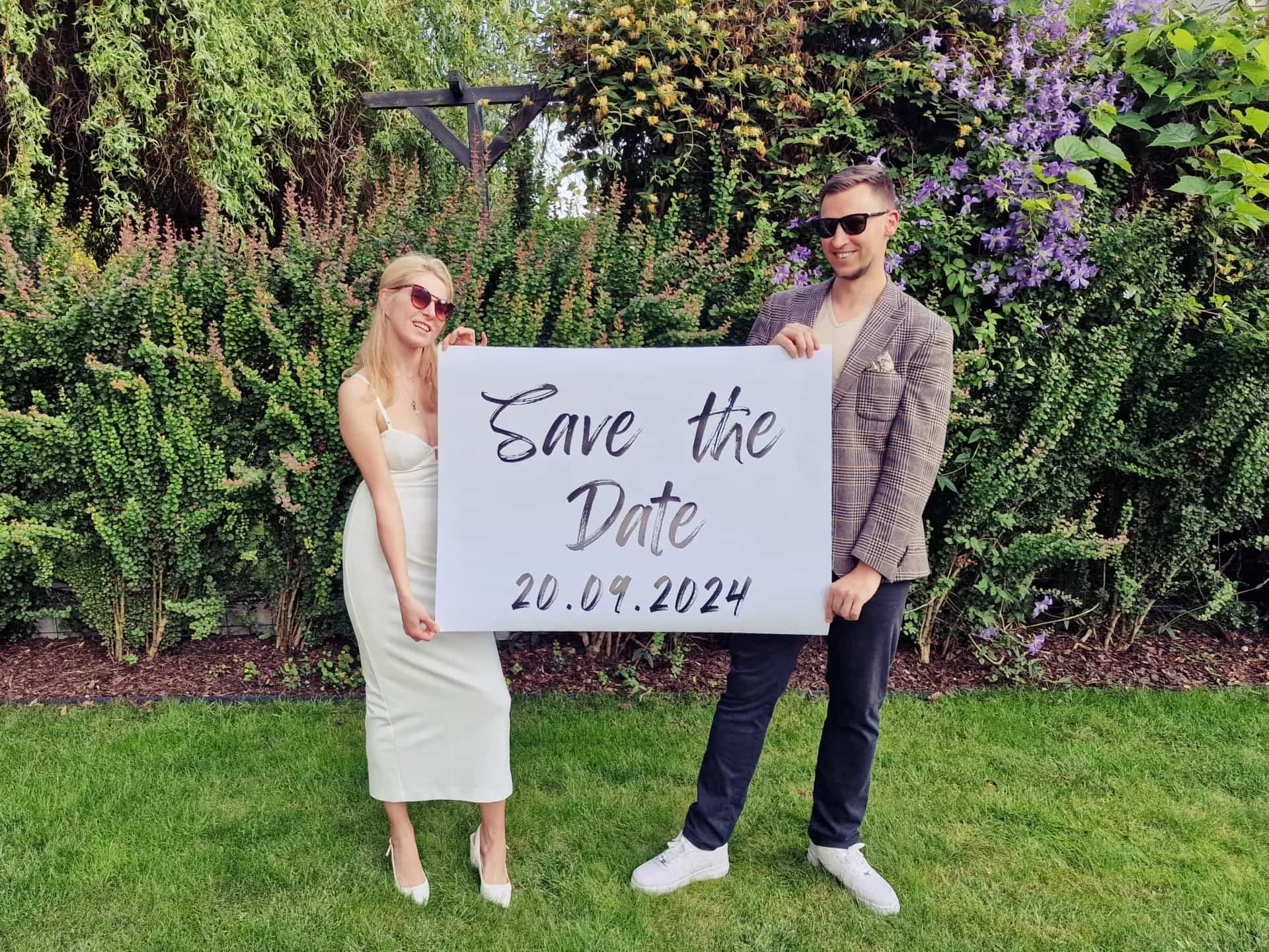 Karolina i Sławek trzymający plakat z napisem "Save the date - 20.09.2024"